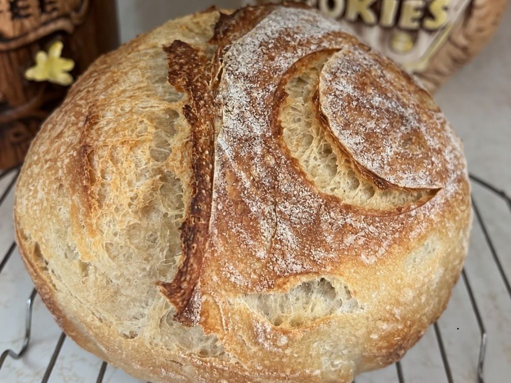 Round sourdough loaf with a crescent-shaped score cooling on a wire rack. 
